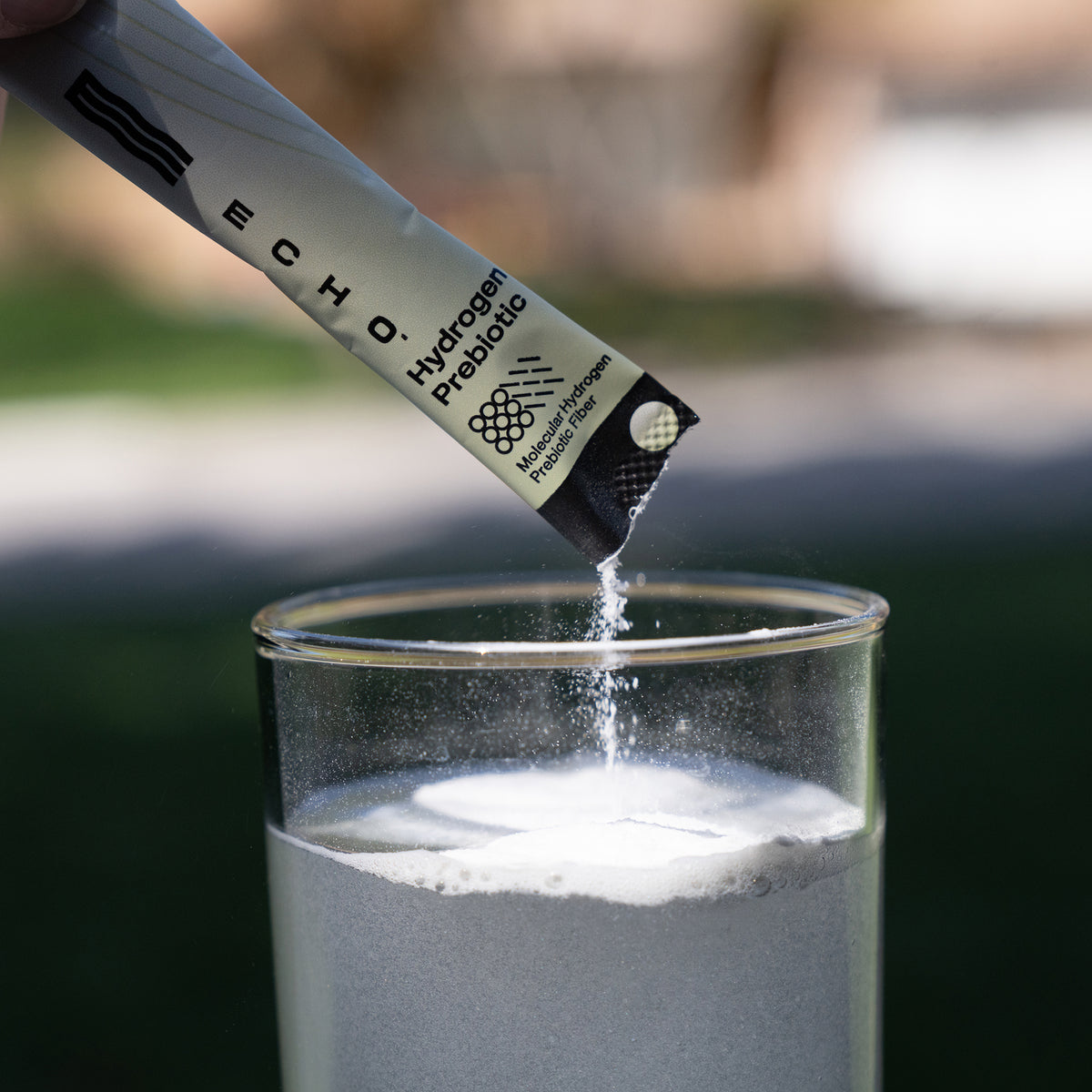 Pouring hydrogen prebiotic powder into a glass of water outdoors