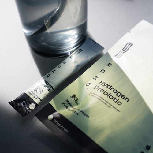 Hydrogen water prebiotic powder stick and packet next to a glass of water in natural light.